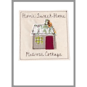 以下が含まれることがあります： 「Home Sweet Home Melrose Cottage」という文字と、赤いドアのある家が刺繍された白いカードです。