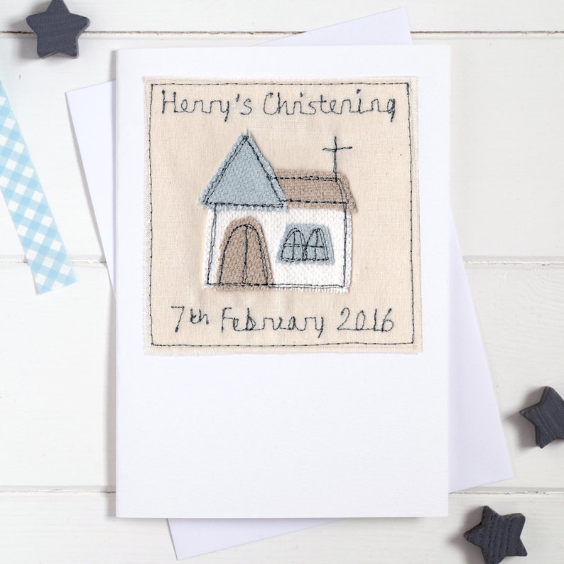 May include: A white card with a beige square patch featuring an embroidered church with a cross on top. The text "Henry's Christening" and "7th February 2016" are embroidered on the patch.