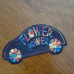 May include: A blue denim patch with colorful embroidery that reads "Flower Power" and features two stylized flowers.