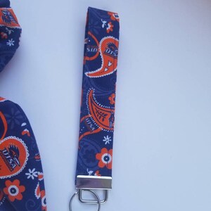 May include: A blue and orange paisley patterned fabric keychain with a silver key ring. The fabric features the text "UTSA Roadrunners" repeated throughout the design.