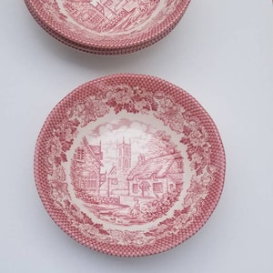 May include: A set of four pink and white ceramic bowls with a vintage floral design. The bowls feature a detailed illustration of a village scene with a church and houses.
