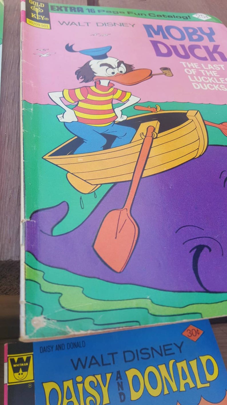 May include: A vintage comic book cover featuring Donald Duck as Moby Duck, rowing a boat on a purple whale. The cover is pink with green and white accents. The title reads "Moby Duck" and "The Last of the Luckles Ducks".