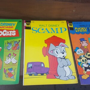 May include: Three vintage Walt Disney comic books featuring the characters Aristocats, Scamp, and Daisy and Donald. The covers are yellow, green, and orange with illustrations of the characters.