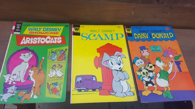 May include: Three vintage Walt Disney comic books featuring the characters Aristocats, Scamp, and Daisy and Donald. The covers are yellow, green, and orange with illustrations of the characters.