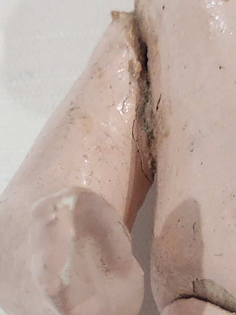May include: Close-up of a pink porcelain doll's arm with a crack running down the side. The doll's arm is bent at the elbow.