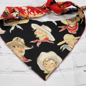 May include: A black bandana with a red border and a pattern of cowboys wearing hats. The bandana is tied in a knot at the top.