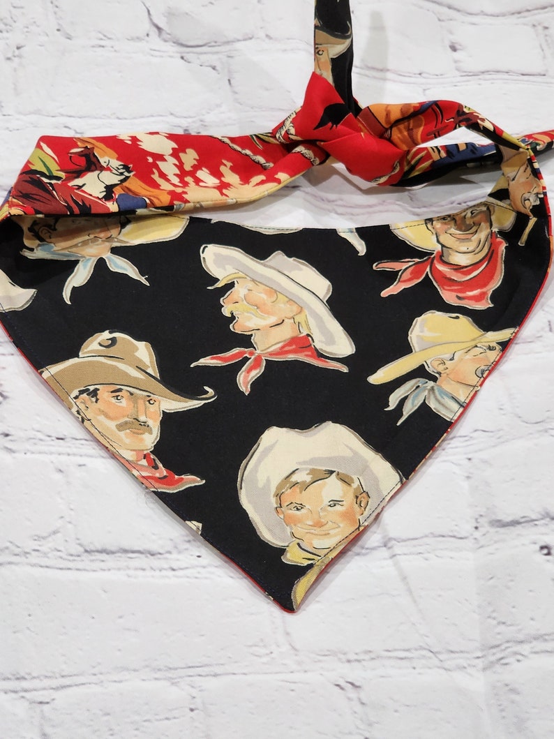 May include: A black bandana with a red border and a pattern of cowboys wearing hats. The bandana is tied in a knot at the top.
