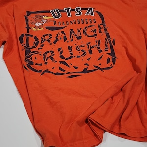 May include: Orange t-shirt with a black and white graphic design featuring a roadrunner and the text "UTSA Roadrunners Orange Crush".