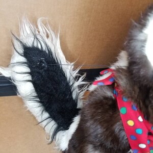 May include: A plush black and white dog toy with a red and white polka dot bandana. The dog has a long, fluffy tail.