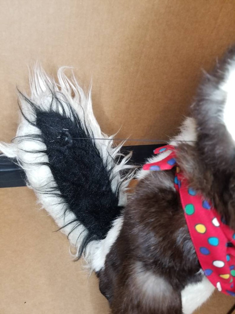 May include: A plush black and white dog toy with a red and white polka dot bandana. The dog has a long, fluffy tail.
