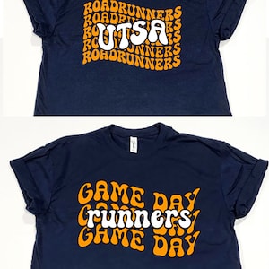 May include: Two navy blue t-shirts with white text and orange outlines. The top shirt has the text "UTSA" with "Roadrunners" repeated around it. The bottom shirt has the text "Game Day" repeated with "Runners" in the middle.
