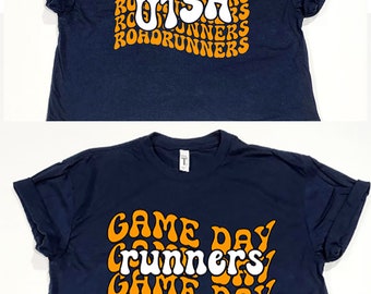May include: Two navy blue t-shirts with white text and orange outlines. The top shirt has the text "UTSA" with "Roadrunners" repeated around it. The bottom shirt has the text "Game Day" repeated with "Runners" in the middle.