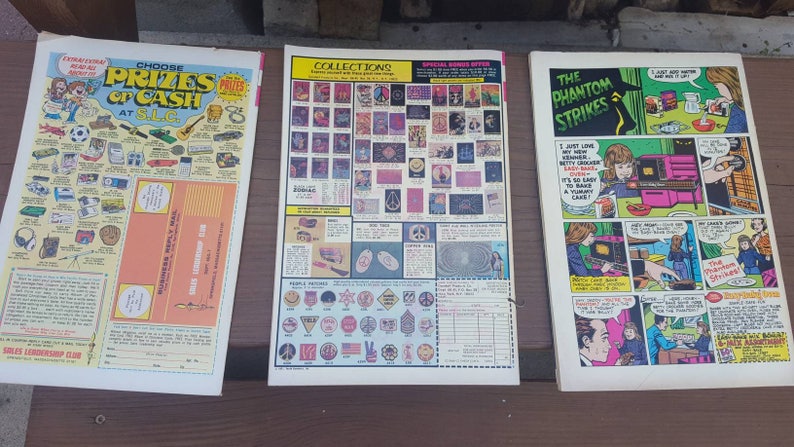 May include: Three comic books with colorful covers. The first comic book has a blue cover with the text "Choose Prizes of Cash at SLC". The second comic book has a red, white, and blue cover with the text "Collections". The third comic book has a red, white, and blue cover with the text "The Phantom Strikes".