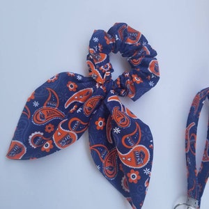 May include: A blue and orange paisley patterned hair scrunchie with a bow and a matching lanyard with a key ring.