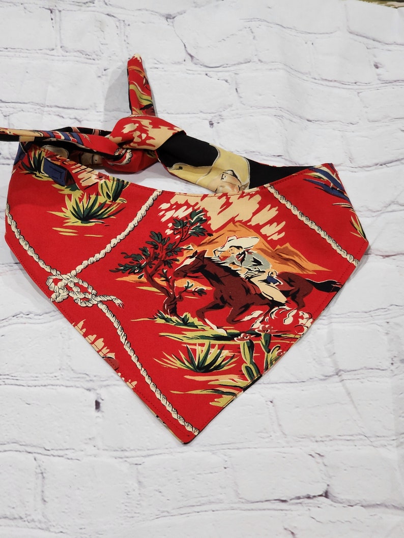 May include: Red bandana with a cowboy riding a horse on a desert landscape. The bandana has a white rope design around the edges.