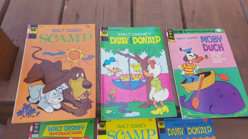 May include: A collection of vintage Walt Disney comic books featuring Scamp, Daisy and Donald, and Moby Duck. The covers are colorful and feature illustrations of the characters.