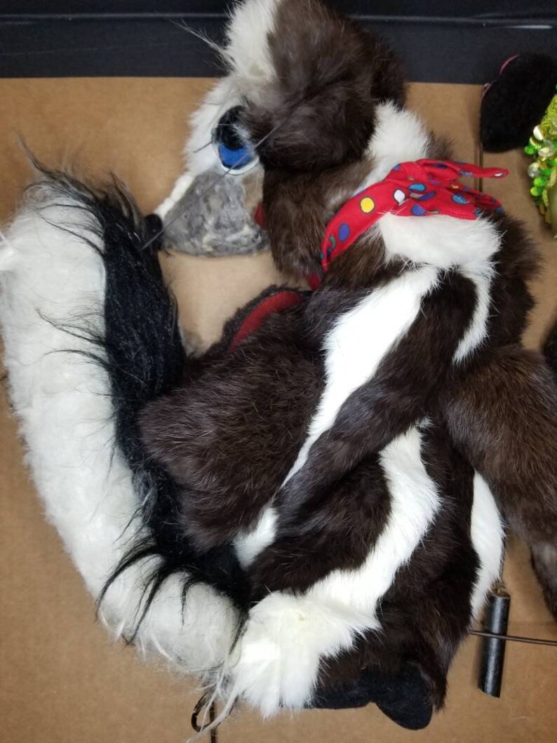 May include: A brown and white skunk puppet with a red and blue bandana around its neck. The puppet has a long, bushy tail and a black nose.
