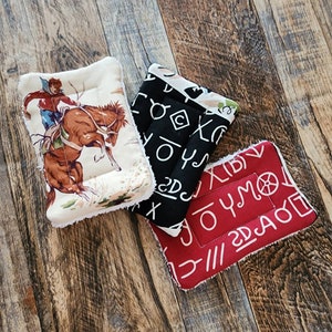 May include: Three pot holders with different designs. One has a cowboy riding a horse, another has black and white letters, and the last one has red with white letters.