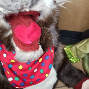 May include: A brown and gray plush toy with a red tongue sticking out. The toy is wearing a red bandana with white, yellow, blue, and green polka dots.