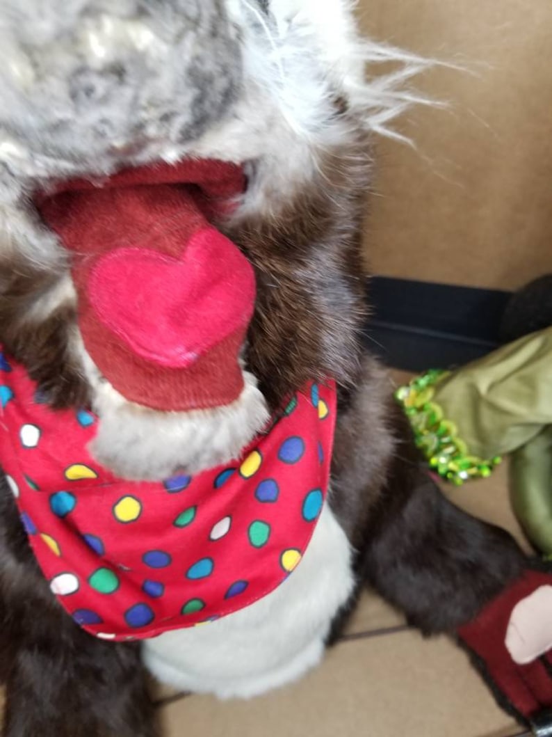May include: A brown and gray plush toy with a red tongue sticking out. The toy is wearing a red bandana with white, yellow, blue, and green polka dots.