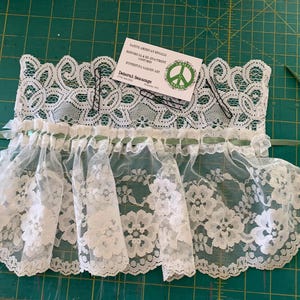 Puede incluir: Borde de encaje blanco con una cinta verde y una tarjeta de visita que dice "Native American Regalia, Historical Re-enactment,  Kythera Garden Art, Deborah Jean Designs".