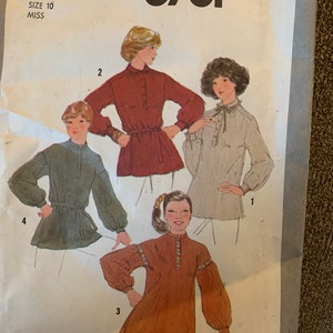 May include: Simplicity sewing pattern number 8781 for a miss size 10. The pattern includes four different styles of blouses with long sleeves. The blouses are shown on four different models. The first blouse is a red blouse with a belt. The second blouse is a light gray blouse with a bow. The third blouse is a brown blouse with a high neck. The fourth blouse is a green blouse with a belt.