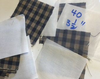 May include: A close-up of fabric squares in a black and tan plaid pattern. The squares are stacked and some are in a plastic bag. The bag has a handwritten note that says "40 1/3"