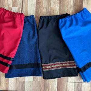 May include: Four drawstring bags in red, blue, black, and denim blue. The red bag has two black stripes, the denim blue bag has a single black stripe, the black bag has a patterned band, and the blue bag has a single black stripe.