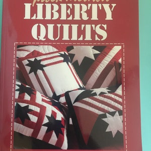 May include: A red book with the title "quick-method LIBERTY QUILTS" in white text. The cover features a photo of red, white, and blue patchwork quilt squares with stars.