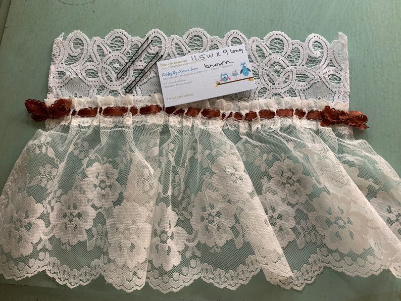 Puede incluir: Borde de encaje blanco con una cinta marr&oacute;n y dos pinzas para el pelo negras. El borde mide 29,2 cm de ancho y 22,9 cm de largo. El texto en la tarjeta dice "Crafty By Nature Blue".