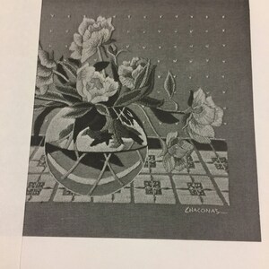 May include: Black and white peony crewelwork design featuring a floral arrangement in a round vase. The vase sits on a patterned surface, with the artist's signature, "ZHACONAS," visible.