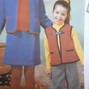 May include: Two girls wearing colorful clothing. The girl on the left is wearing a blue skirt and jacket with a red sweater underneath. The girl on the right is wearing a yellow shirt, red vest, and black and white checkered pants.