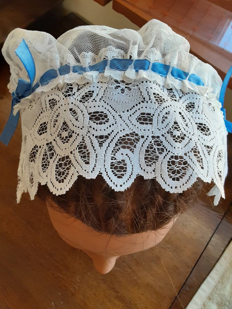 Puede incluir: Bonnet de encaje blanco para el cabello con un ribete de cinta azul. El bonnet se lleva en una cabeza de maniqu&iacute; con cabello casta&ntilde;o.