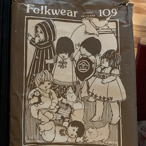 Pode incluir: Padrão Folkwear 109 para bebês e crianças pequenas, com uma ilustração em preto e branco de crianças vestindo roupas tradicionais de diferentes culturas. O padrão inclui instruções para fazer roupas do Marrocos, México, Turquia, Japão e Nepal.
