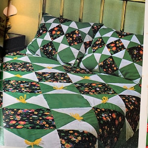 Puede incluir: Una colcha verde y blanca con un patrón floral. La colcha está en una cama con una cabecera de latón. La colcha tiene lazos amarillos en cada esquina.