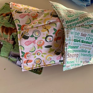 May include: Three fabric pot holders. One is pink with a sushi pattern, one is green with a donkey pattern, and one is white with a Girl Scout motto pattern.