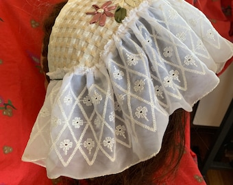 May include: A white lace bonnet with a ruffled edge and a floral embroidered design on the top. The bonnet is made of a sheer fabric and has a delicate, feminine look.