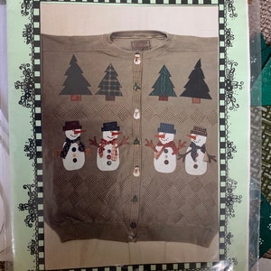 May include: A brown sweater with a plaid pattern and four appliqued snowmen. The sweater has a button-up front and the text "Snowy Day" is printed on the bottom.