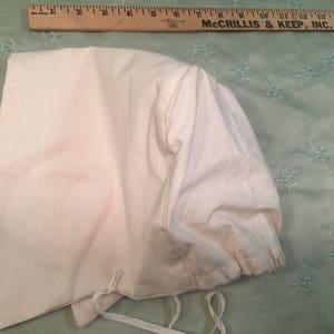 Puede incluir: Un gorro blanco de algodón con un borde fruncido y un cierre de cordón. El gorro está hecho de una tela suave y ligera, perfecto para el uso diario.