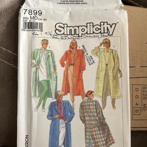 May include: A Simplicity 7899 sewing pattern envelope in size MD (14-16). The front features illustrations of long coats in various colors and patterns, including green stripes, solid orange, and a multi-colored plaid, worn over pants and shirts.