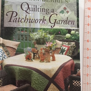 May include: A book titled "Quilting a Patchwork Garden" by Lynette Jensen, featuring a cover image of a garden scene with a table set with a patchwork quilt and decorative bunny figurines.