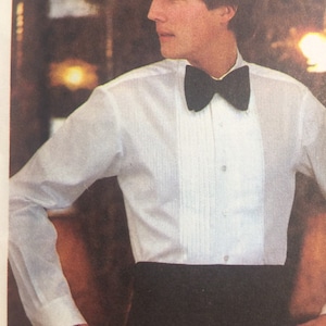 May include: A white long-sleeved dress shirt featuring a pleated front panel, a classic collar, and a solid black bow tie. The shirt is paired with a high-waisted black cummerbund that sits at the waistline, creating a formal and structured appearance.