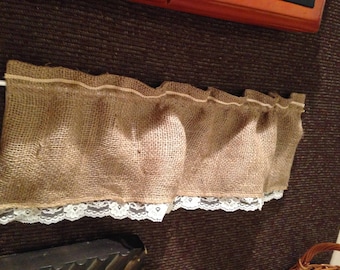 May include: A brown burlap valance with a white lace trim. The valance is hung on a white rod.