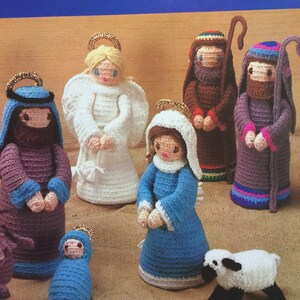 May include: Crocheted nativity scene with figures of Mary, Joseph, baby Jesus, an angel, shepherds, and a lamb. The figures are made with white, blue, purple, brown, and pink yarn.