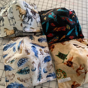 May include: Four square fabric bowl cozies with various patterns. One features running horses, another black with colorful feathers, a third with blue and brown feathers, and the last with Native American figures. Each has a small tag.