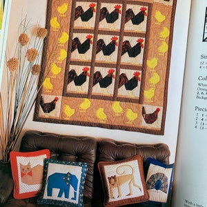 Puede incluir: Una colcha con fondo marrón y un patrón repetido de gallos negros y pollitos amarillos. La colcha está colgada en una pared sobre un sofá de cuero marrón con tres almohadas. Las almohadas están decoradas con un gato, un elefante y un león.