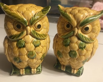 May include: A pair of ceramic owl salt and pepper shakers. The owls are yellow with green accents and have black eyes. They are standing on green bases.