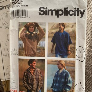 May include: Simplicity sewing pattern number 9226 for a pullover with a zipper. The pattern includes four different styles of the pullover, including a blue plaid, a brown patterned, a blue solid, and a black and white patterned pullover. The pattern is for sizes XS, S, and M.
