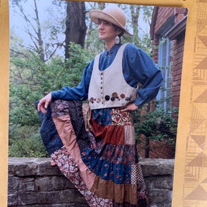 May include: A photograph of a woman wearing a tiered patchwork skirt and a beige vest adorned with floral embellishments. The outfit is paired with a denim shirt and a straw hat. The text "Tiered Skirt & Yo-Yo Vest" is visible at the top.