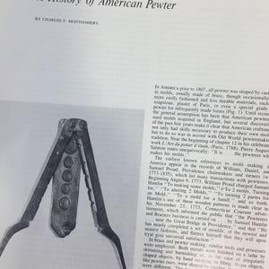 Op de afbeelding: Een zwart-witfoto van een paar antieke tinnen tangen. De tangen staan open en de handvatten zijn van hout. De tangen worden gebruikt om tin te vormen.